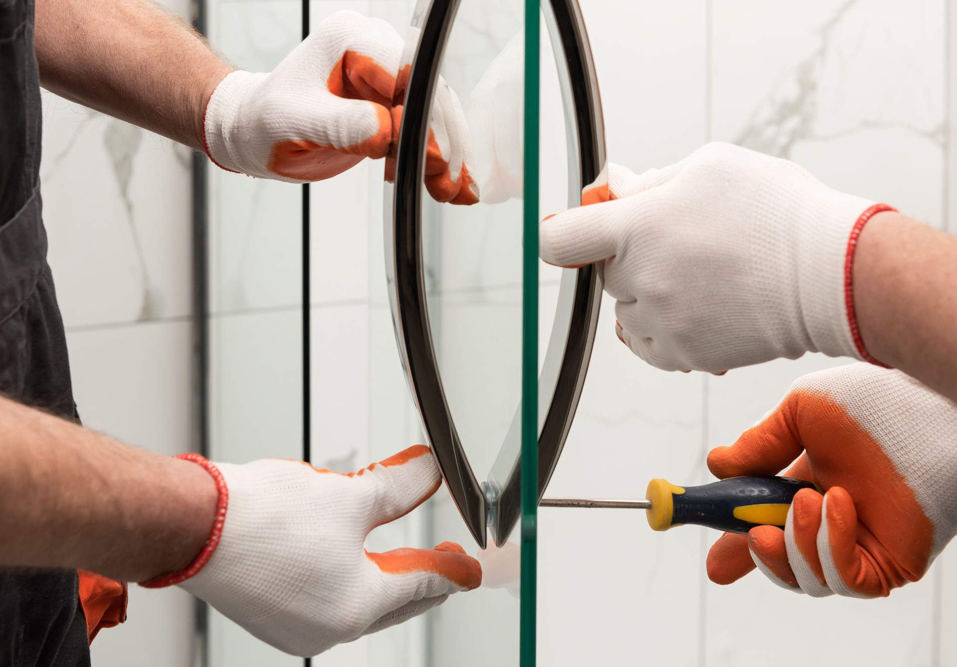 Technicians wearing gloves installing a glass shower door with screwdrivers — representing clean, expert installation.